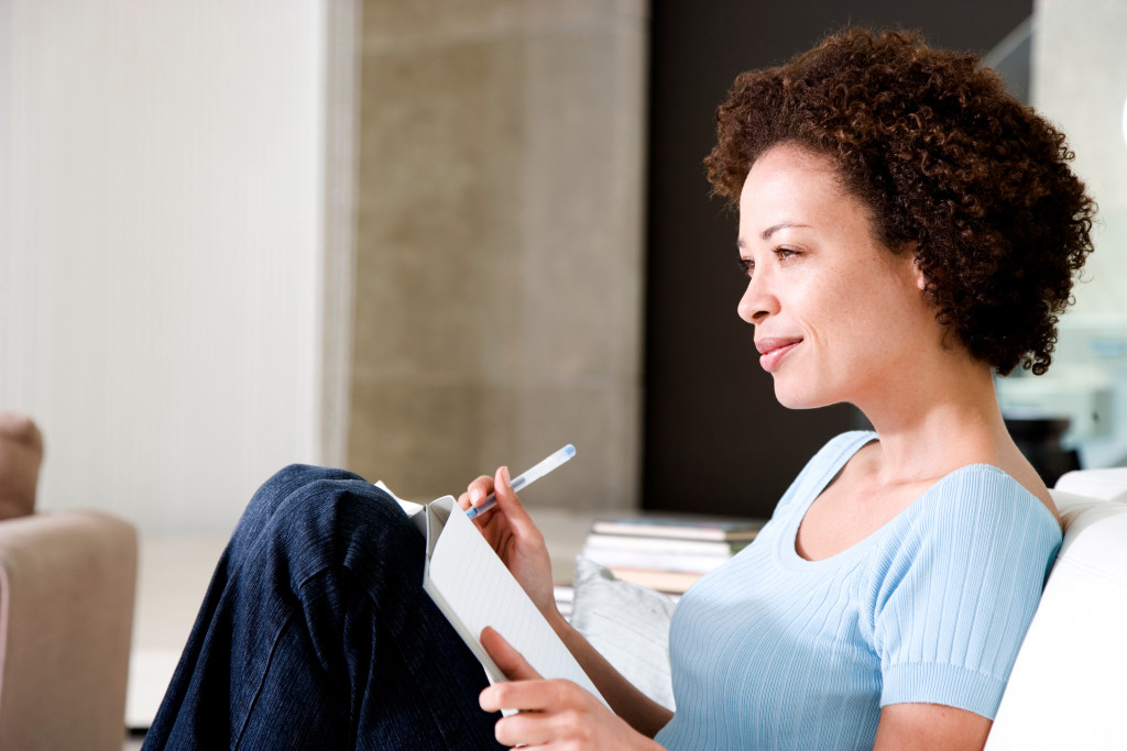 curly haired woman smiling while thinking of what to write in journal at home