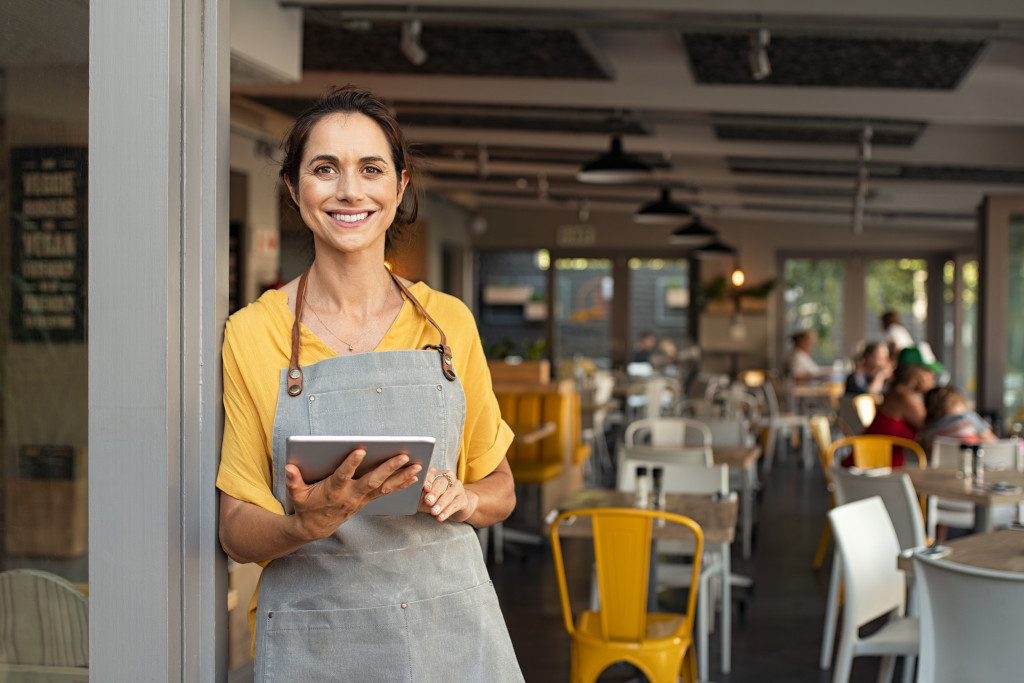 Young woman smiling while standing at the doorway of her restaurant.